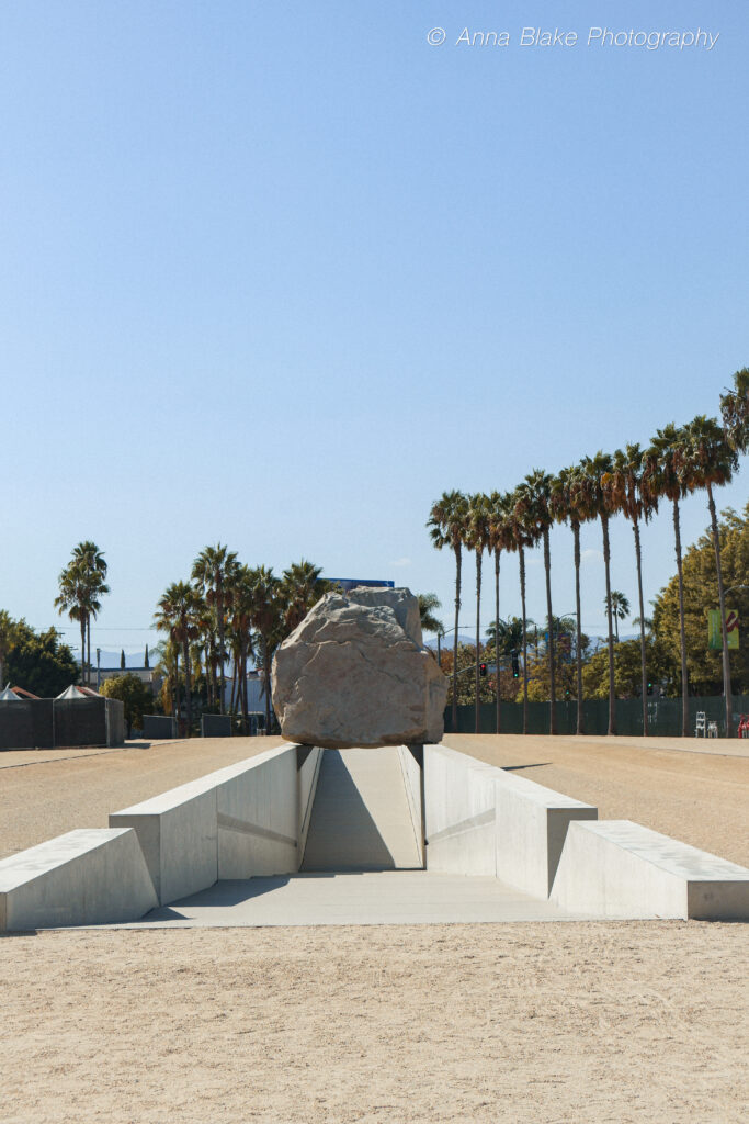 A giant rock sitting on an underpass walkway with palm trees in the background