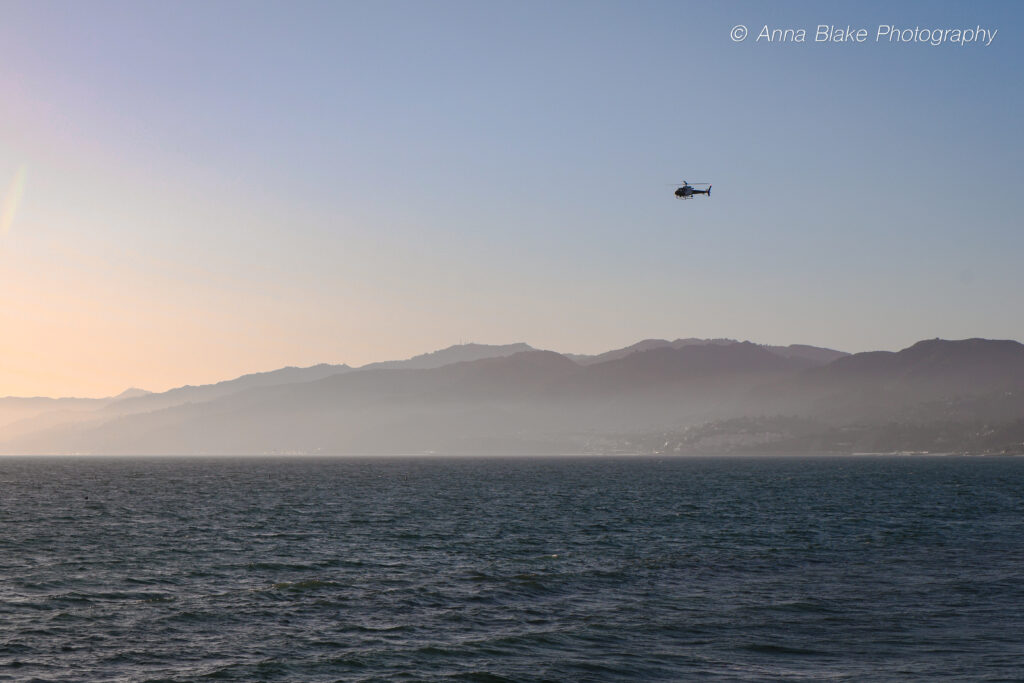 Sunset landscape of mountains and Pacific Ocean with a helicopter flying in the distance
